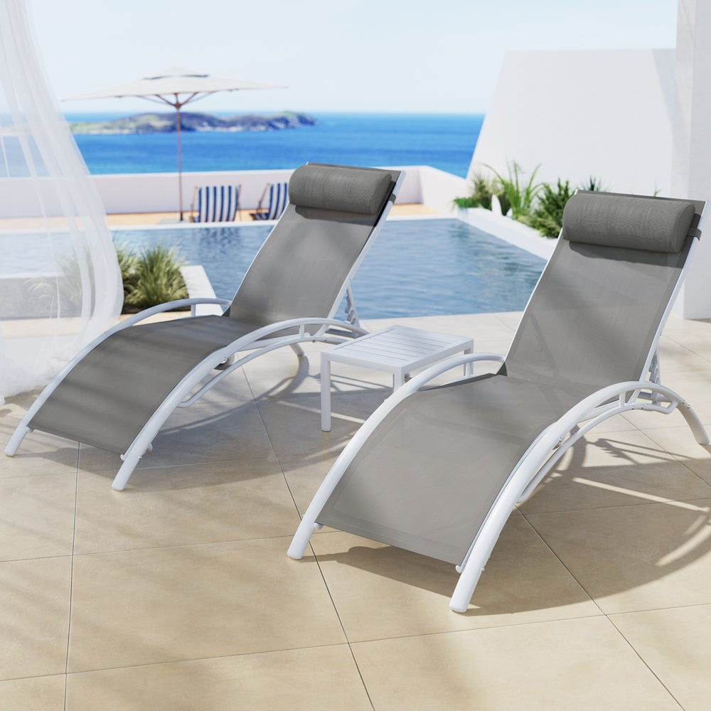 Two gray lounge chairs on a patio with a pool and ocean view.