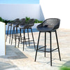 A set of four black Gardeon outdoor bar stools with plastic seats and metal frames, set in a row on a tiled surface in an outdoor poolside setting.