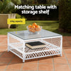 White matching table with storage shelf on a patio, featuring a bowl of oranges and a book.