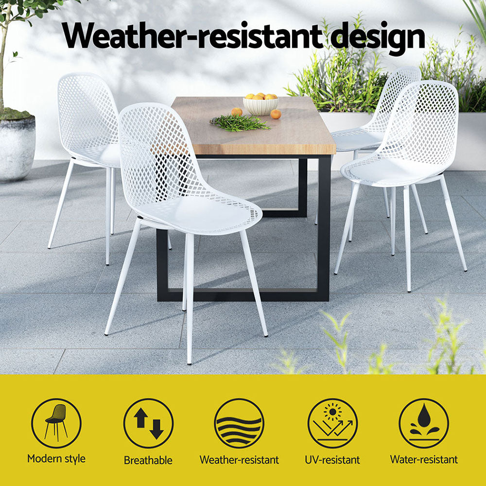Gardeon 4PC Outdoor Dining Chairs in White around a rectangle wood top table with black metal legs set on a tiled surface with a wall and plants in the backdrop.