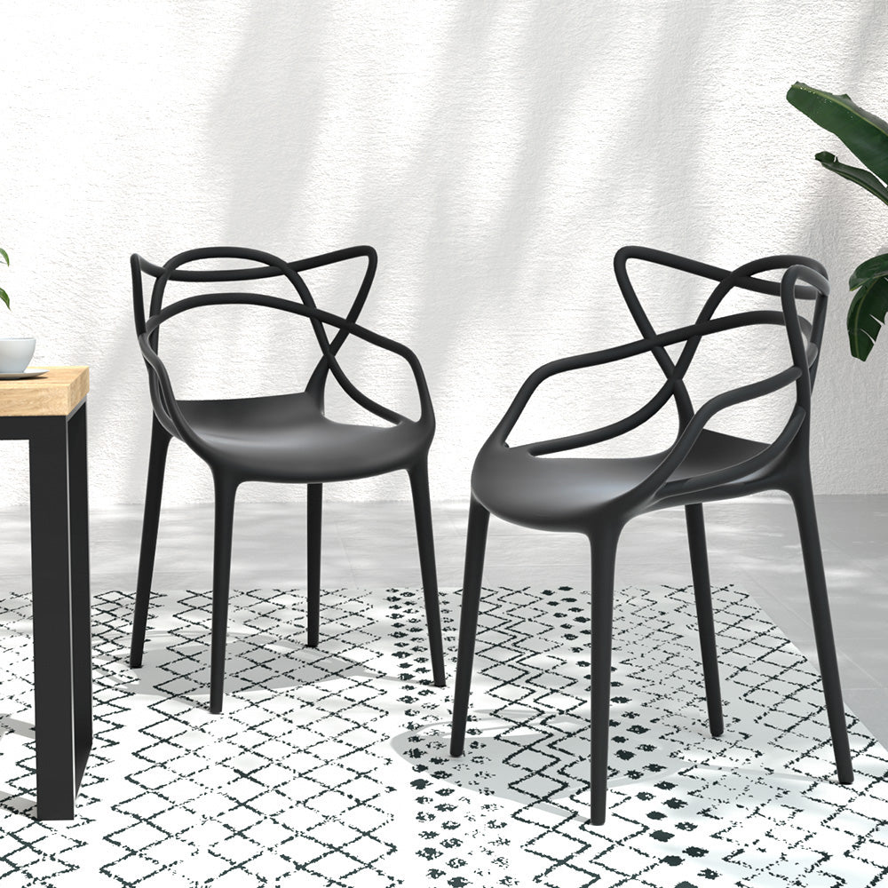 Two black, stackable outdoor dining chairs with curved backrests facing each other and slightly to the side and set on a tiled surface on a black and white floor mat in front of a white wall.