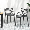 Two black, stackable outdoor dining chairs with curved backrests facing each other and slightly to the side and set on a tiled surface on a black and white floor mat in front of a white wall.