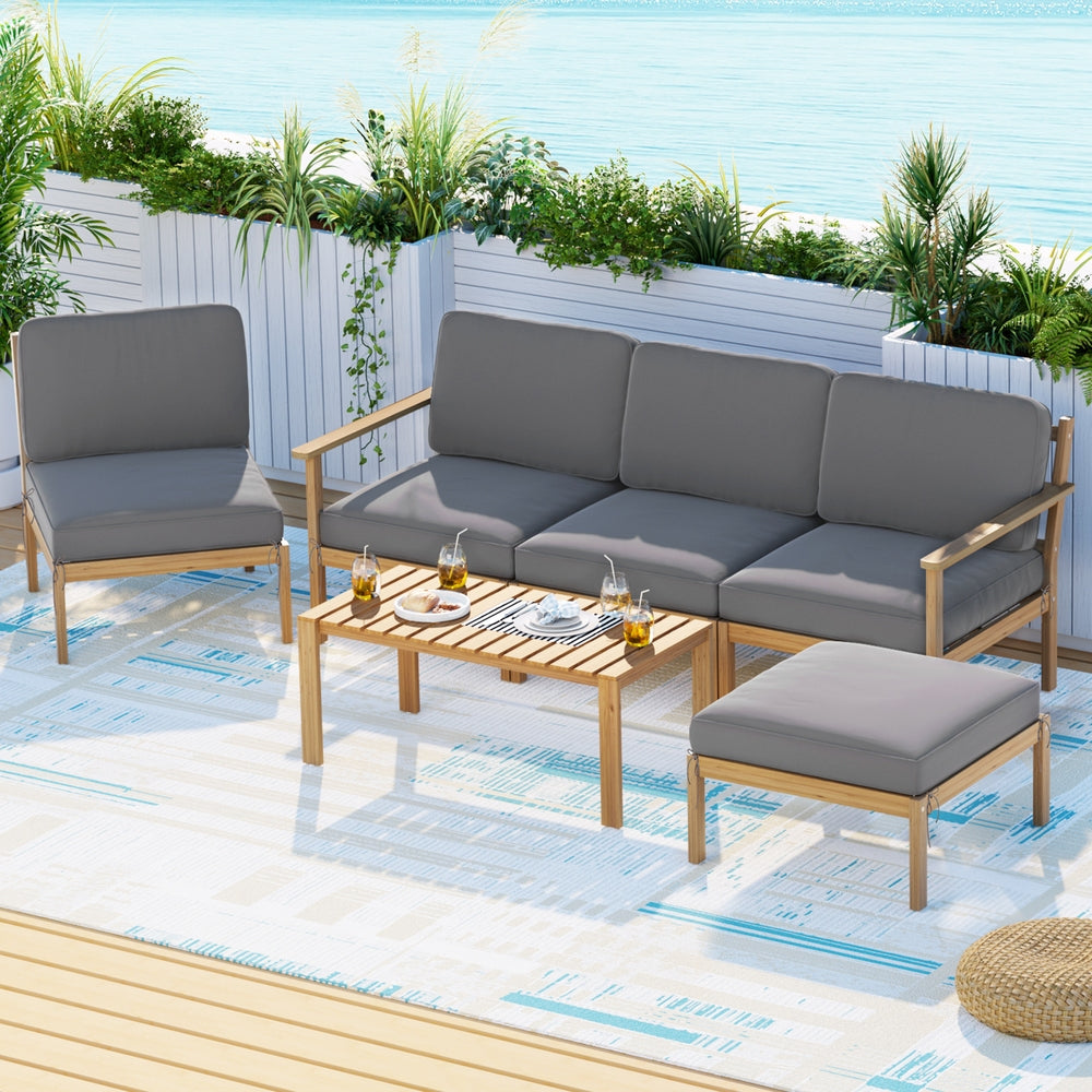 Outdoor furniture set with gray cushions on a patio with plants and a blue sky.