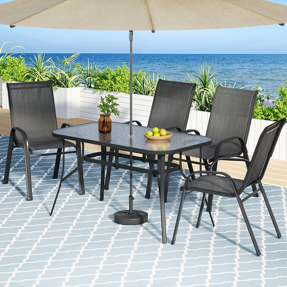 Outdoor dining set with table and chairs under a large umbrella on a tiled patio with ocean view.