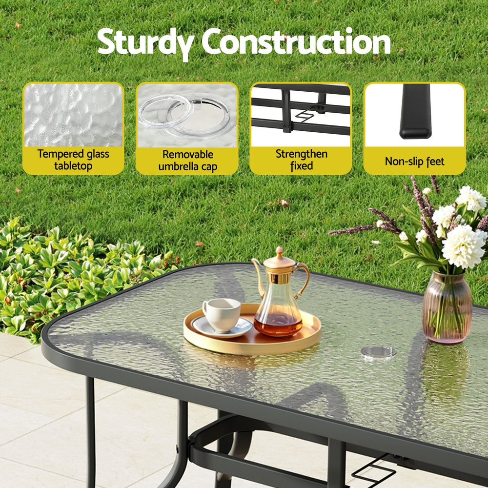 Outdoor table with tempered glass top, removable umbrella cap, strengthened fixed parts, and non-slip feet on a grassy background.