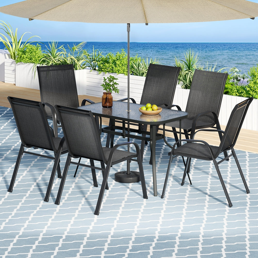 Outdoor dining set with table and chairs under a large umbrella on a patio with ocean view.