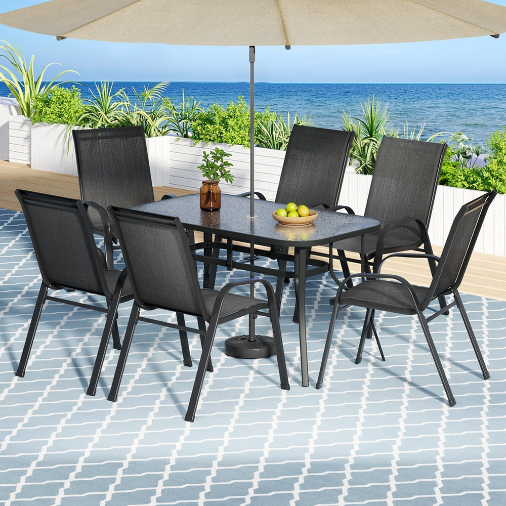 Outdoor dining set with table and chairs under an umbrella on a patio with ocean view.