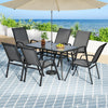 Outdoor dining set with table and chairs under a large umbrella by the sea.