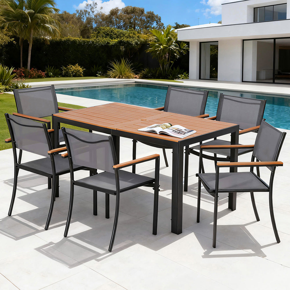 Outdoor dining set with wooden table and gray chairs by a poolside.