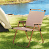 A Gardeon portable folding beach chair made of steel with a beige oxford fabric seat, set beside a tent on a grass bank at a lake side.