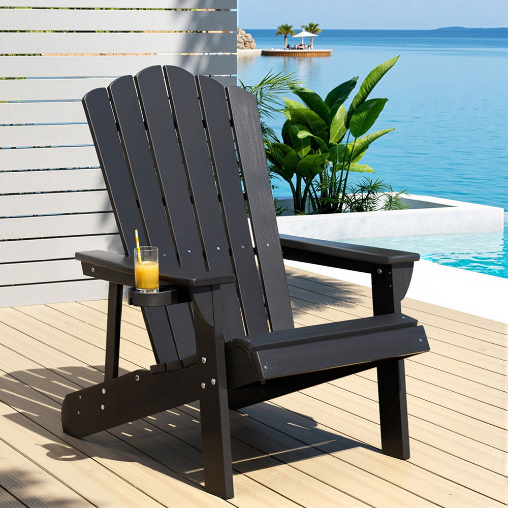 Black Adirondack chair on a wooden deck with a view of a pool and water.