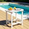 White folding table by a pool with oranges, a glass of juice, and a newspaper.