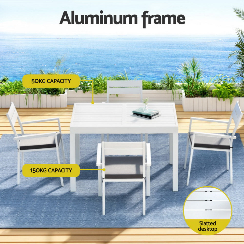 Outdoor dining set with white table and chairs on a deck with ocean view, labeled 'Aluminum frame' and 'Slatted desktop'.