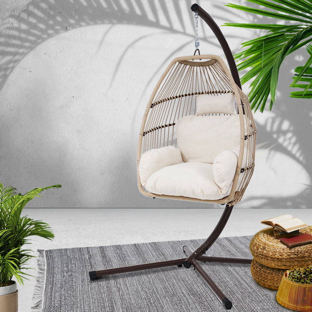 Hanging chair with white cushions on a stand, surrounded by plants and a rug.