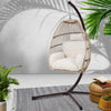 Hanging chair with white cushions on a stand, surrounded by plants and a rug.