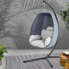Hanging egg-shaped chair with stand in a room with plants and a rug.
