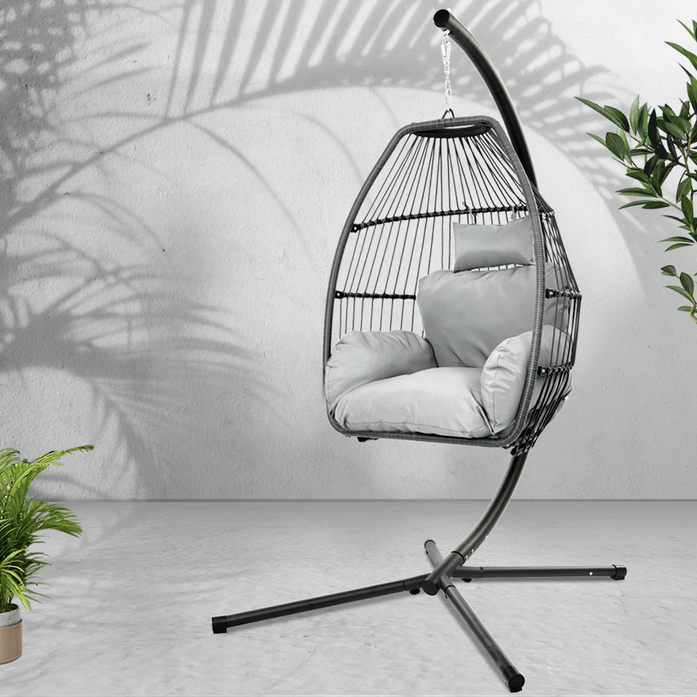 Hanging chair with cushions on a stand against a light gray wall with plants around.