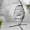 Hanging chair with cushions on a stand against a light gray wall with plants around.