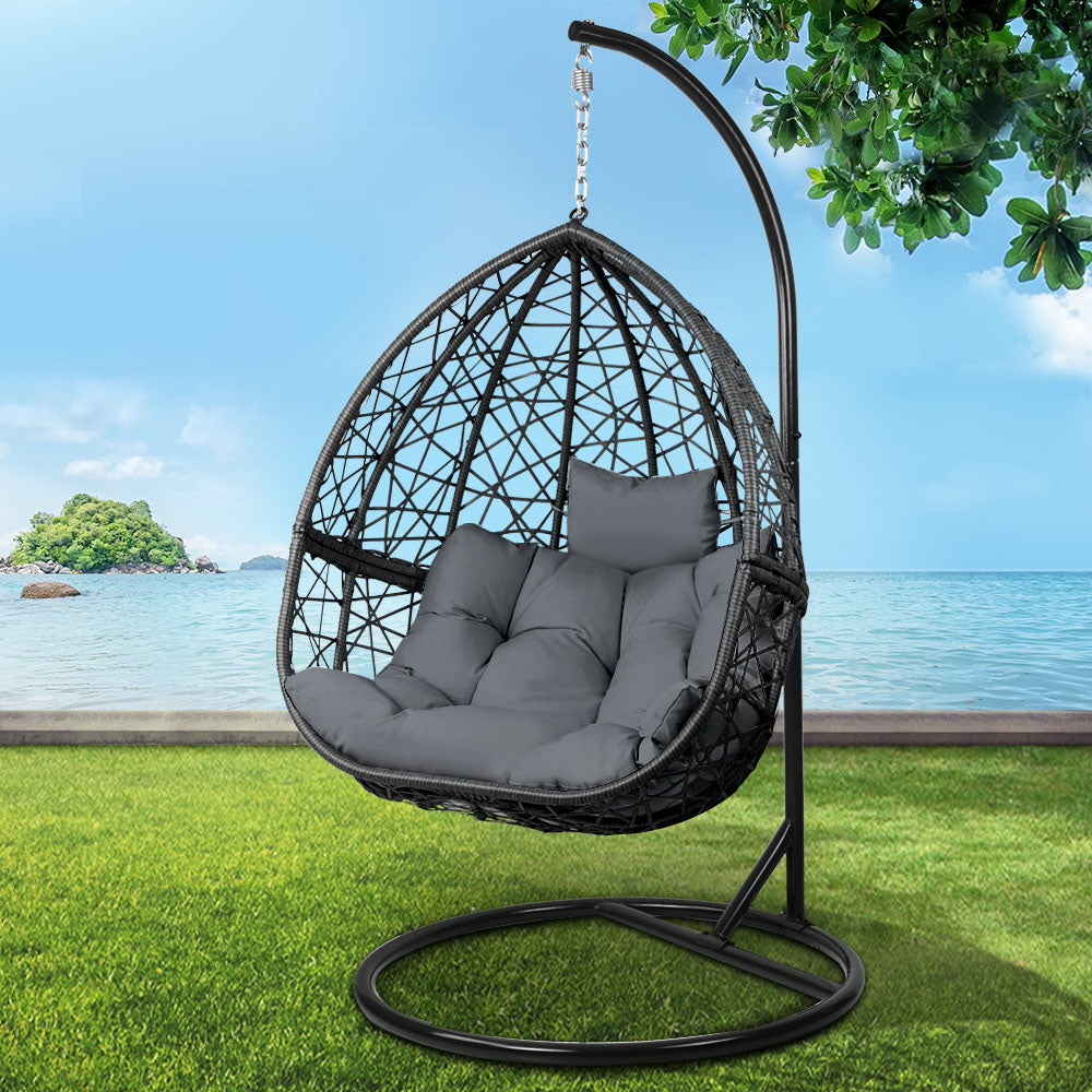 Hanging egg chair with gray cushions on a stand in a garden setting with ocean view