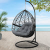Hanging egg chair with gray cushion on a stand outdoors with a beach view.