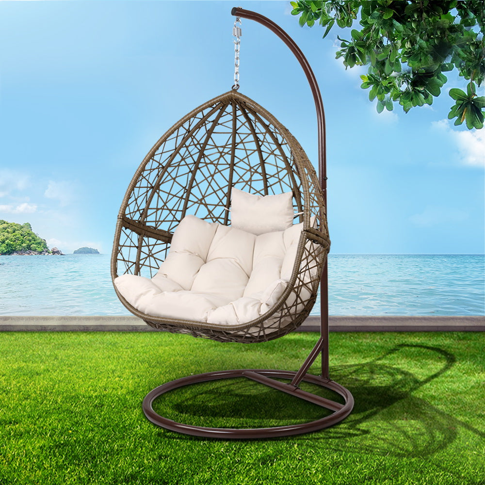 Hanging chair with white cushions on a grassy area with a scenic background