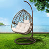 Hanging chair with white cushions on a grassy area with a scenic background