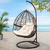 Hanging egg chair with white cushion on a stand outdoors with plants and ocean view