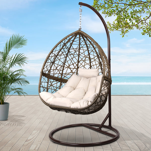 Hanging egg chair with white cushion on a stand outdoors with plants and ocean view