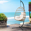 Wicker hanging chair with white cushions on a wooden deck by the ocean.