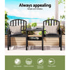 A two-seater garden bench set with a black steel frame, featuring an all-in-one table and armchairs, cushions on the seats, a plant pot on the table and books on the shelf under the table, set in front of a window overlooking an ocean view.