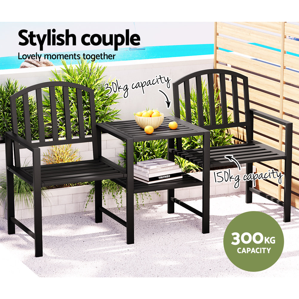 A two-seater garden bench set with a black steel frame, featuring an all-in-one table and armchairs, a bowl of fruits on the table and books on the shelf beneath the table, set on a balcony that is overlooking an ocean view with a boat in the background.