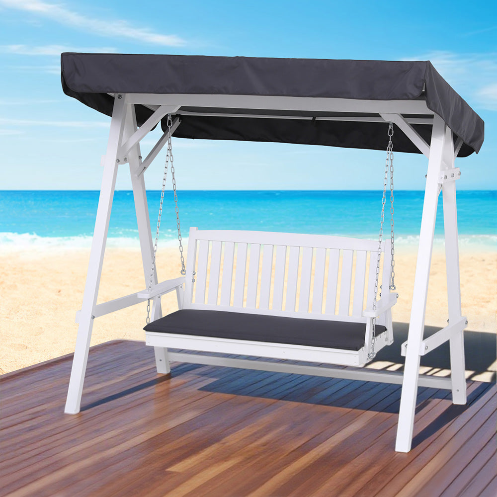 White swing bench with black canopy on a wooden deck by the beach
