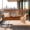 Wooden swing on a balcony with a city skyline view, pillows, and a blanket.