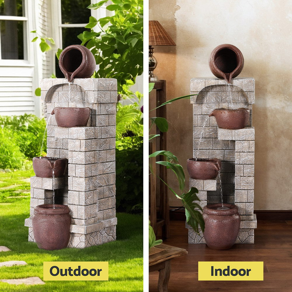 Split images showing inddor and outdoor views of a brown, four-tier cascading water bowls fountain feature. set against a textured wall and made from polyresin. Outdoor photo is set on a green lawn with a house and greenery in the background. Indoor photo is near a cream wall, on wooden flooring with a tall lamp table and lamp standing beside it and two pot plants.