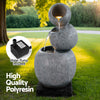 A three-tier bowls cascading water fountain feature with LED lights, made of polyresin, in a grey colour with black base, insert image of the water pump included, all in a garden setting with trees in the background.