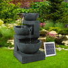 A blue three-tier cascading water feature with bowls, set in a garden before a brick wall on green lawn area with trees, rockery and flower bed in the background.