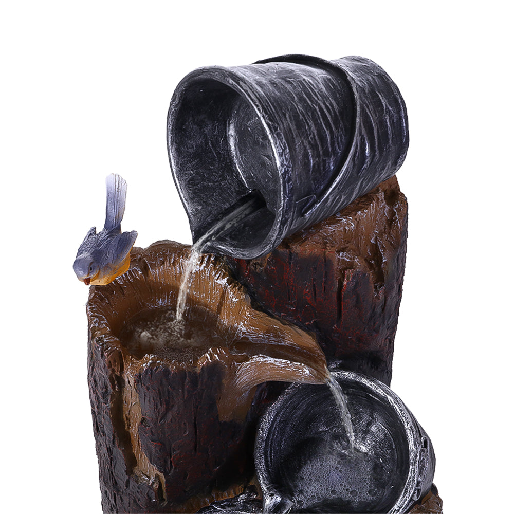 A close up of the top of a 3-tier cascading fountain featuring buckets and tree stump that pour into each other, with a bird sitting on the tree stump. The fountain is set against a white background.