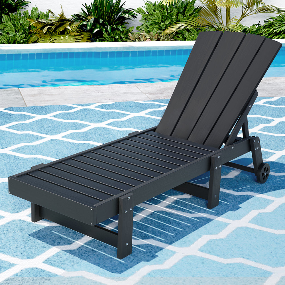 Black lounge chair on a pool deck with pool and plants in the background
