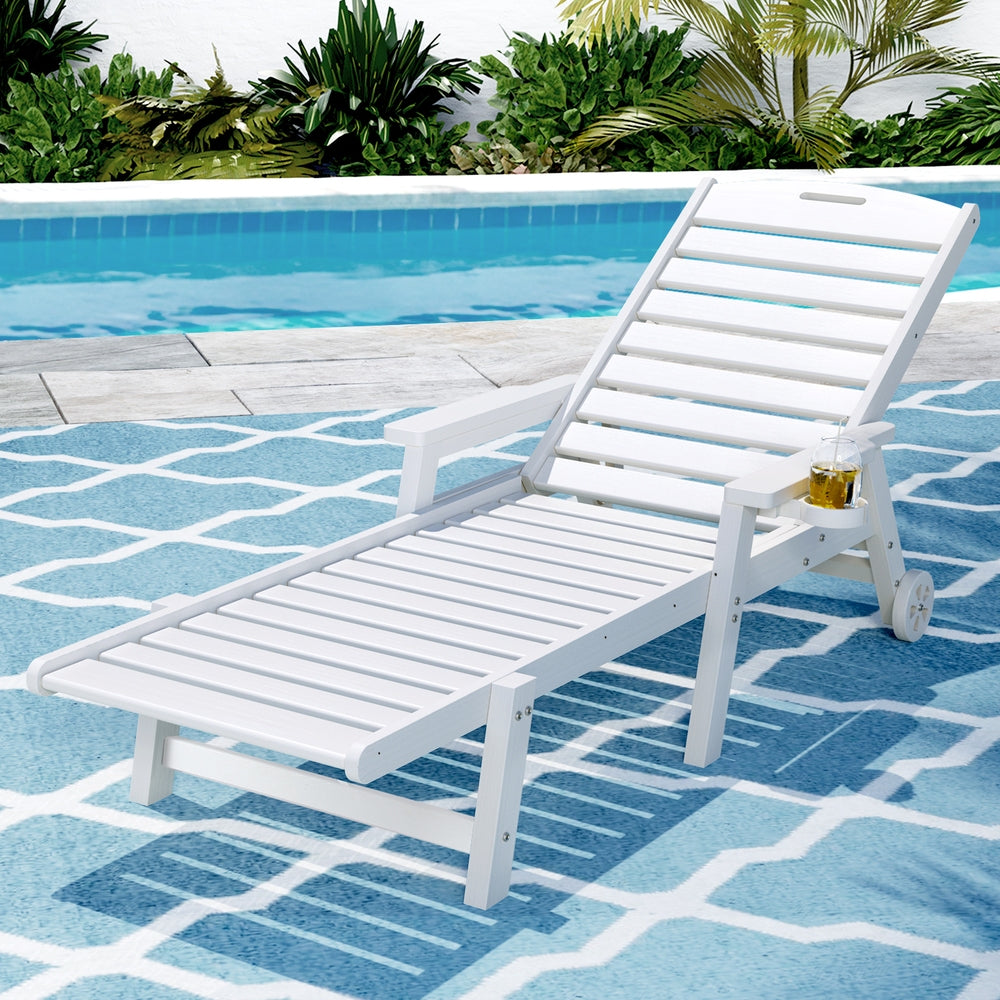 White lounge chair on a blue and white patterned rug by a pool with greenery in the background