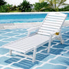 White lounge chair on a blue and white patterned rug by a pool with greenery in the background