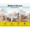 Two white Gardeon folding sun loungers with wheels, in 2 different reclining positions with a small matching table in between them with a couple of glasses of red wine, set on a wood deck with beach in the background.