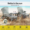 Two grey Gardeon folding sun loungers with wheels, in 2 different reclining positions with a small matching table in between them with a couple of glasses of red wine, set on a wood deck with beach in the background.