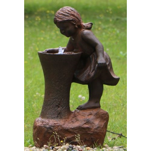 Girl at Water Fountain in a garden setting with pebbles, and green grass with dandelions surrounding it.