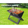 A black Grillz Foldable BBQ Grill Charcoal Smoker with steaks, kebabs, and tomatoes set on a lawn with bushes and flowers in the background.