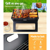 A black Grillz Foldable BBQ Grill Charcoal Smoker cooking steak, sausages, kebabs and corn cobs, set on a table with condiments and grass, picnic rug and basket in the background. Close-up inserted image of the BBQ's construction.