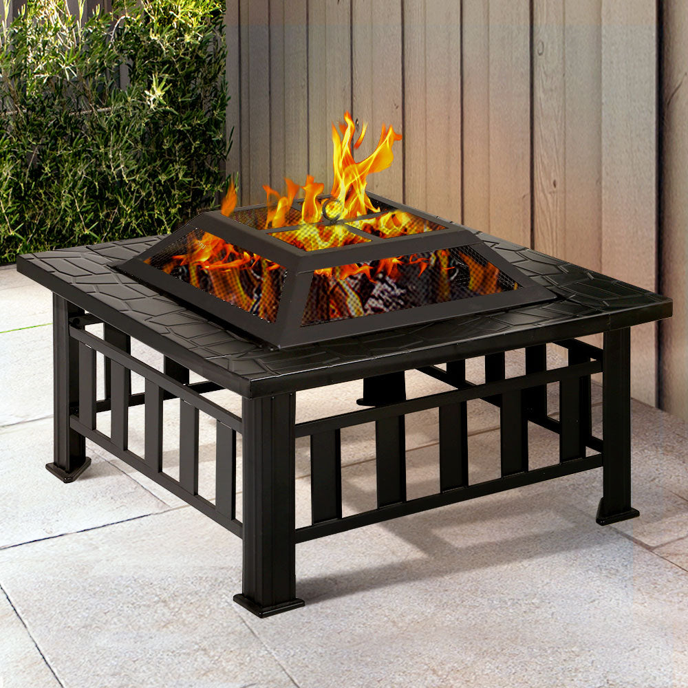 A black 2-in-1 steel Grillz fire pit with a fire burning and a mesh dome on top in an outdoor garden area.