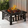 A black 2-in-1 steel Grillz fire pit with a fire burning and a mesh dome on top in an outdoor garden area.