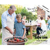 A man cooking on BBQ grill, with his arm around a young boy, both and smiling and family can be seen sitting behind them at a picnic table in a garden setting with house and trees in the background.