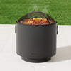 Black cylindrical fire pit with grill grate on a grassy background