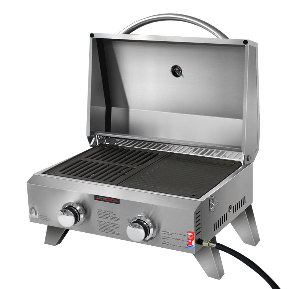A portable stainless steel BBQ grill with two burners, a closed lid, and a carrying handle.